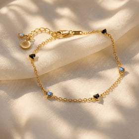 A yellow gold vermeil bracelet lies across cream fabric with a clasp and spaced heart shaped stones.