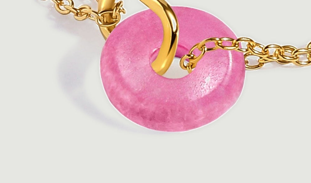 The pink quartz pendant lies at an angle beside yellow gold links on a light gray surface.