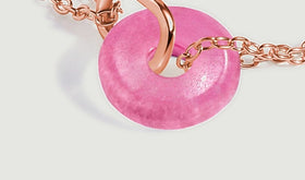Rose gold links curve beside the pink quartz circle in a close view on a gray surface.