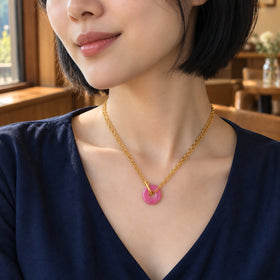 A woman in a navy V-neck blouse wears the pink quartz pendant on two yellow gold chains beside a cafe window.