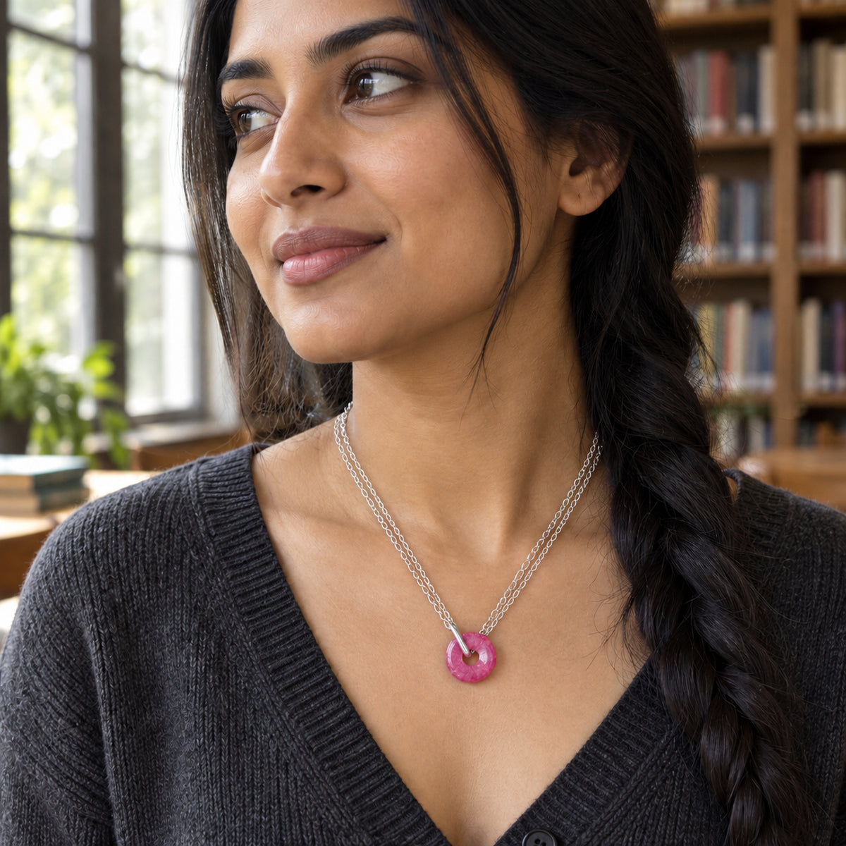 A woman with a side braid wears the circular pink quartz pendant on double silver chains in a library.