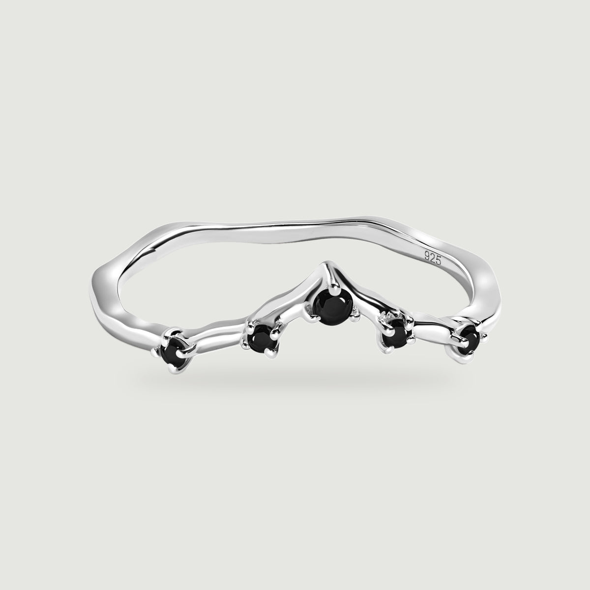 A silver ring with a gently pointed band and five black stones is centered on pale gray.