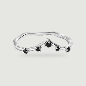 A silver ring with a gently pointed band and five black stones is centered on pale gray.