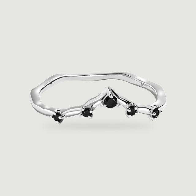 A silver ring with a gently pointed band and five black stones is centered on pale gray.