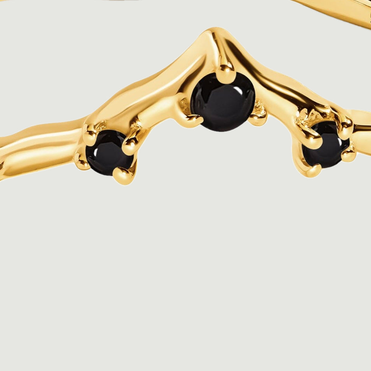Three round black stones sit in polished yellow gold prongs along the pointed front of the ring.