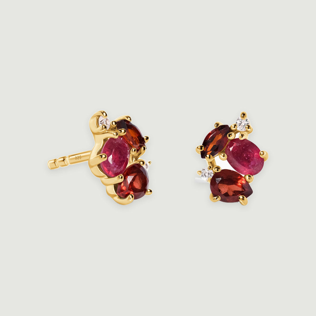 A pair of yellow gold vermeil stud earrings has pink and deep red stones beside small clear accents on a light grey background.