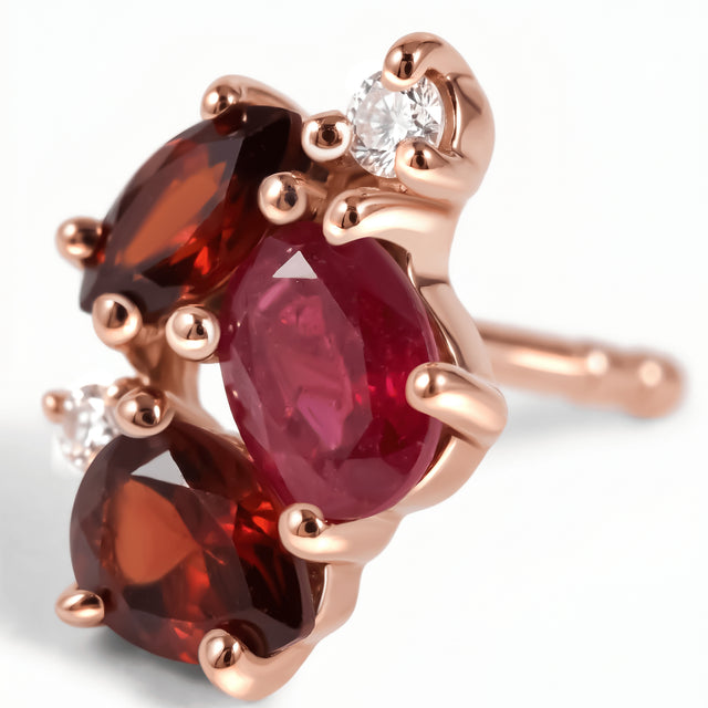 Pink and dark red stones sit in rose gold prongs beside a clear round accent in this close view of an earring.