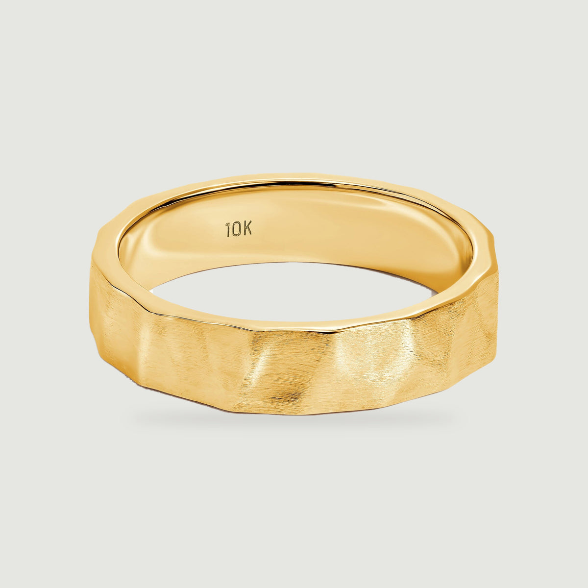 A yellow gold ring with a brushed faceted exterior and polished inner band rests on a light gray surface.