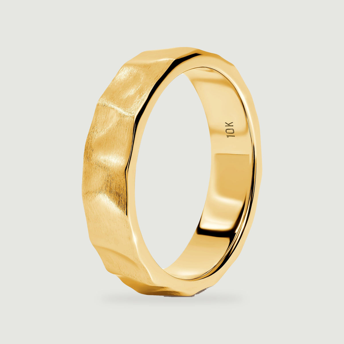 The yellow gold ring stands at an angle, revealing its faceted outer edge and smooth interior.