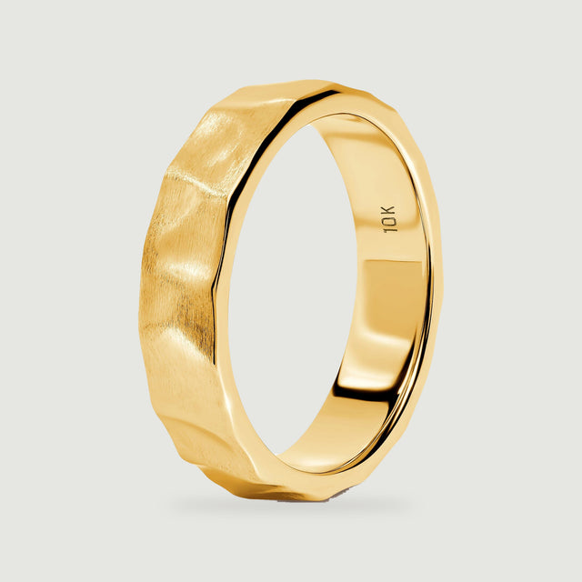 The yellow gold ring stands at an angle, revealing its faceted outer edge and smooth interior.