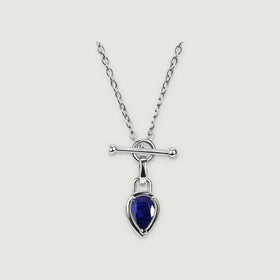 A silver-tone necklace with a deep blue pear-shaped pendant rests on a light gray background.
