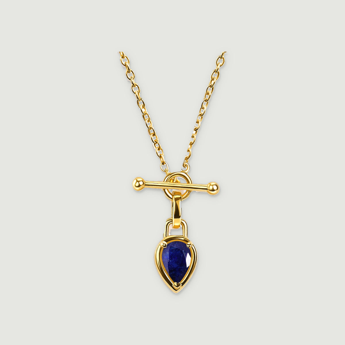 A gold-tone chain and blue pear-shaped pendant are centered on a light gray surface.