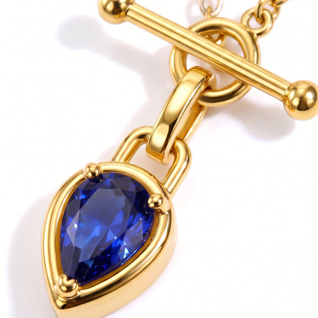 A close view shows a faceted blue pendant beneath a polished gold-tone bar and circular clasp.