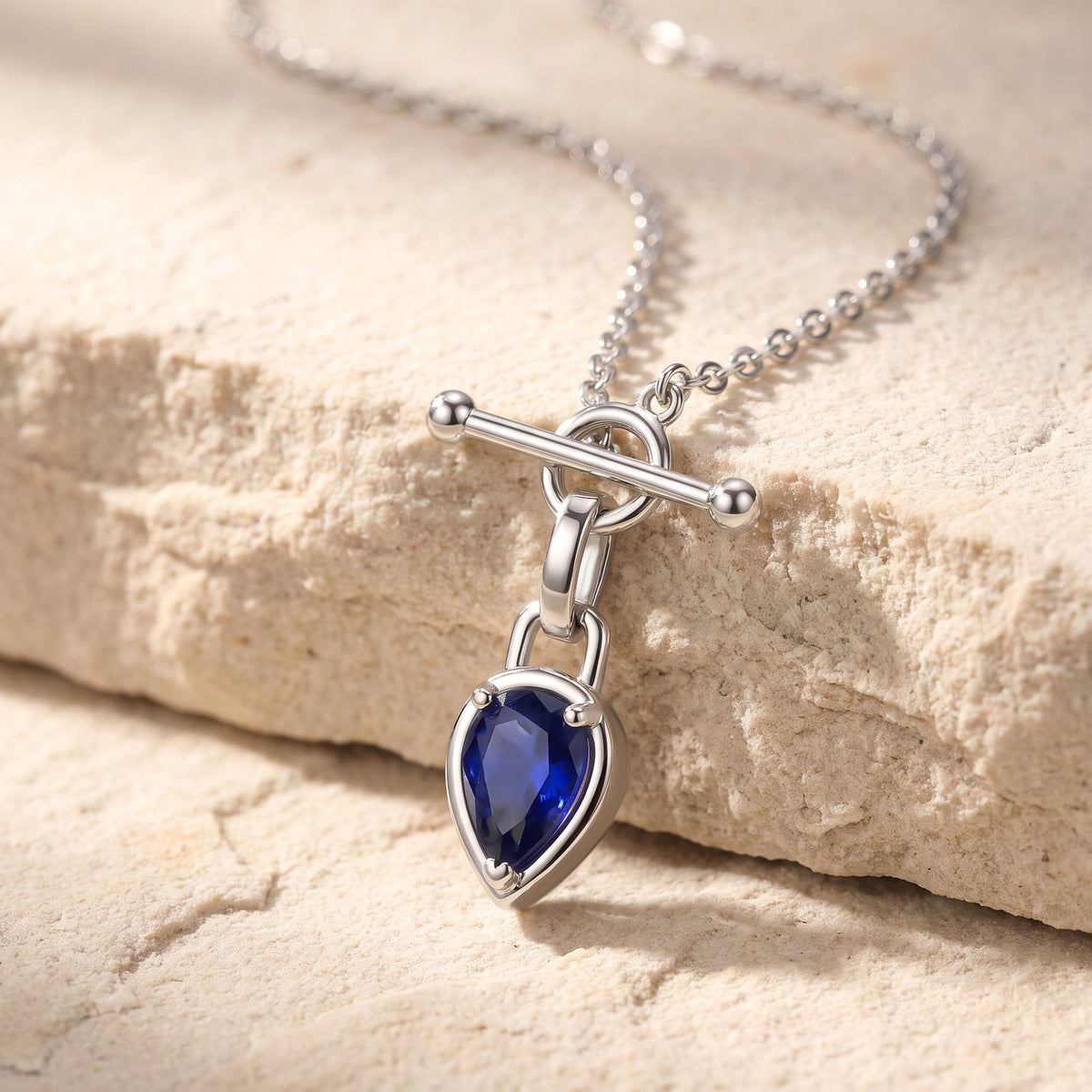 A silver-tone necklace drapes across pale stone with its blue pendant hanging over the edge.