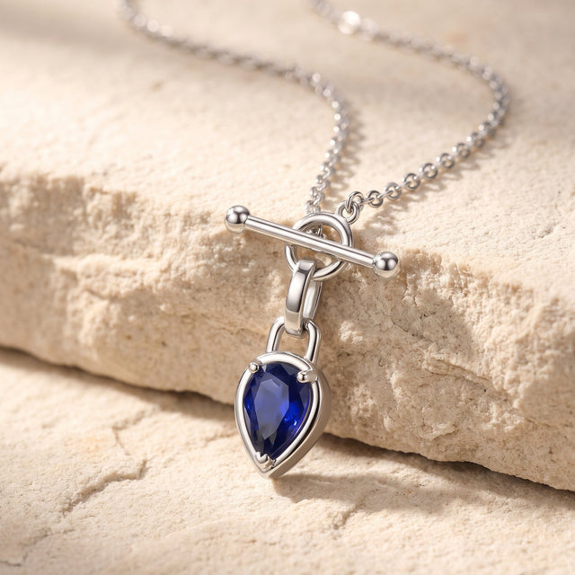 A silver-tone necklace drapes across pale stone with its blue pendant hanging over the edge.