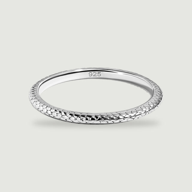 A polished silver ring with a scale-textured band rests on a light gray surface.