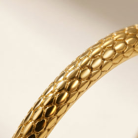 Warm light catches the raised scale pattern along a yellow gold ring band.