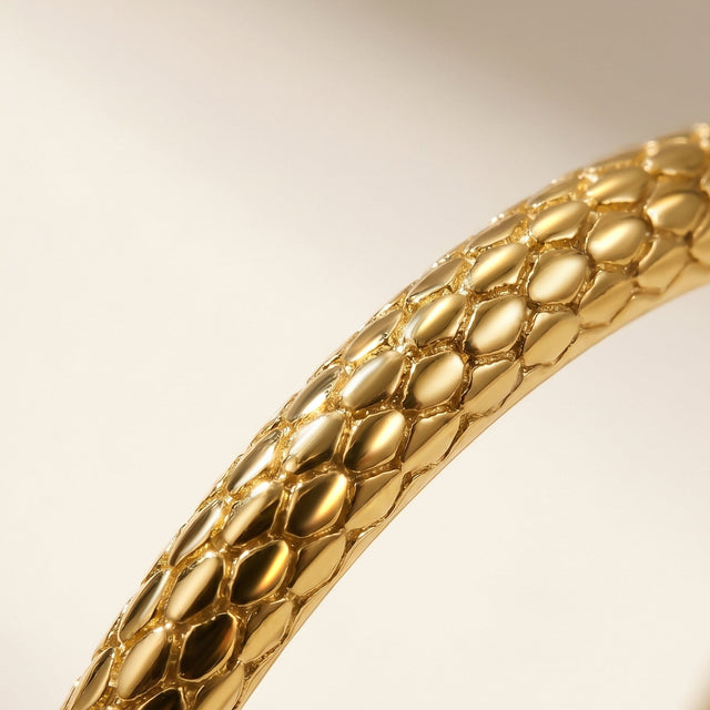 Warm light catches the raised scale pattern along a yellow gold ring band.