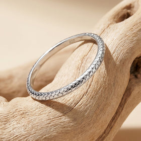 A silver ring rests at an angle on pale wood with its textured band and inner 925 mark visible.