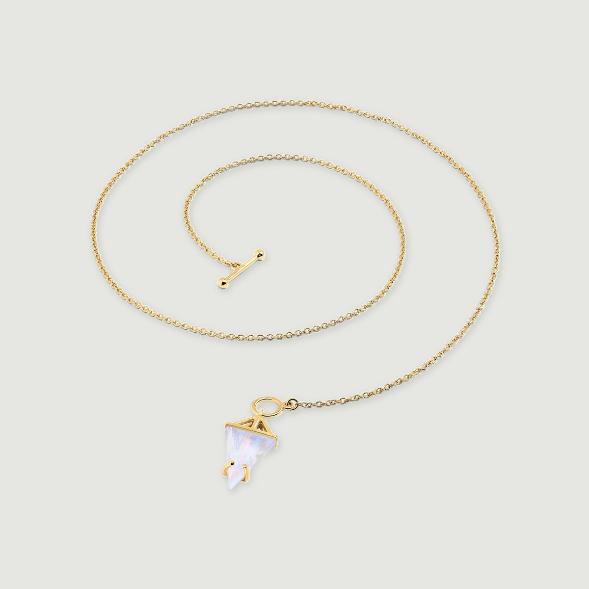 A yellow gold vermeil chain curves around a pointed moonstone pendant and a separate rounded toggle bar on a light gray surface.