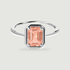 A sterling silver ring with a rectangular peach coral stone is centered on a light gray background.
