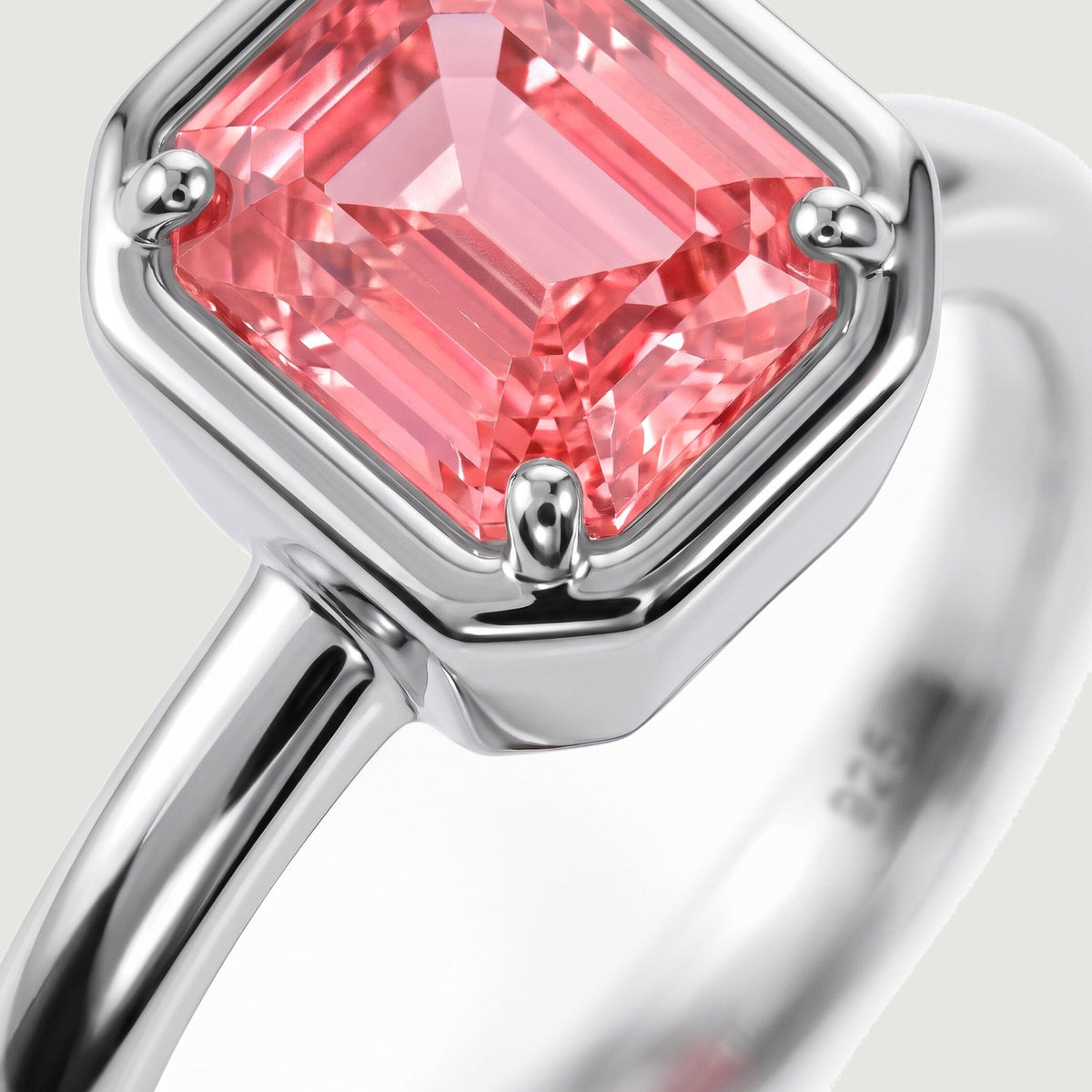 A close view shows the coral pink stone facets and rounded silver prongs above the polished ring band.