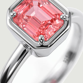A close view shows the coral pink stone facets and rounded silver prongs above the polished ring band.