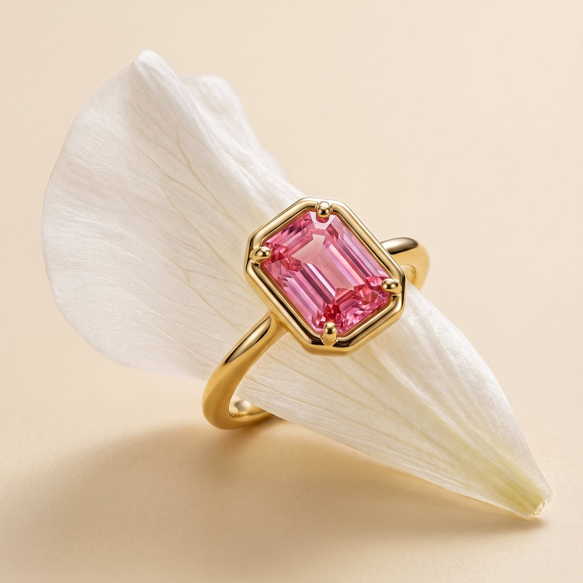 A yellow gold vermeil ring with a rectangular pink coral stone rests across a white flower petal.