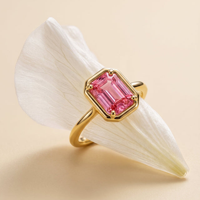 A yellow gold vermeil ring with a rectangular pink coral stone rests across a white flower petal.