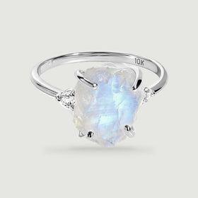 A white gold ring with four rounded prongs frames a blue-flashing rough moonstone and two side diamonds.