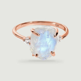 A rose gold ring displays a translucent rough moonstone, two round diamonds, and a slim polished band.