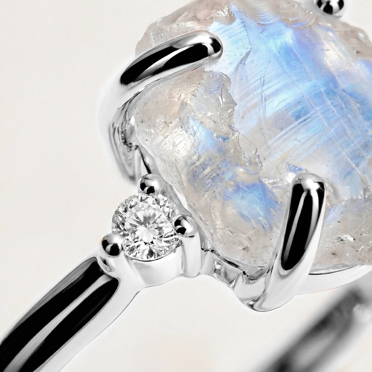 The white gold setting and a diamond accent appear beside the uneven surface and pale blue sheen of the moonstone.