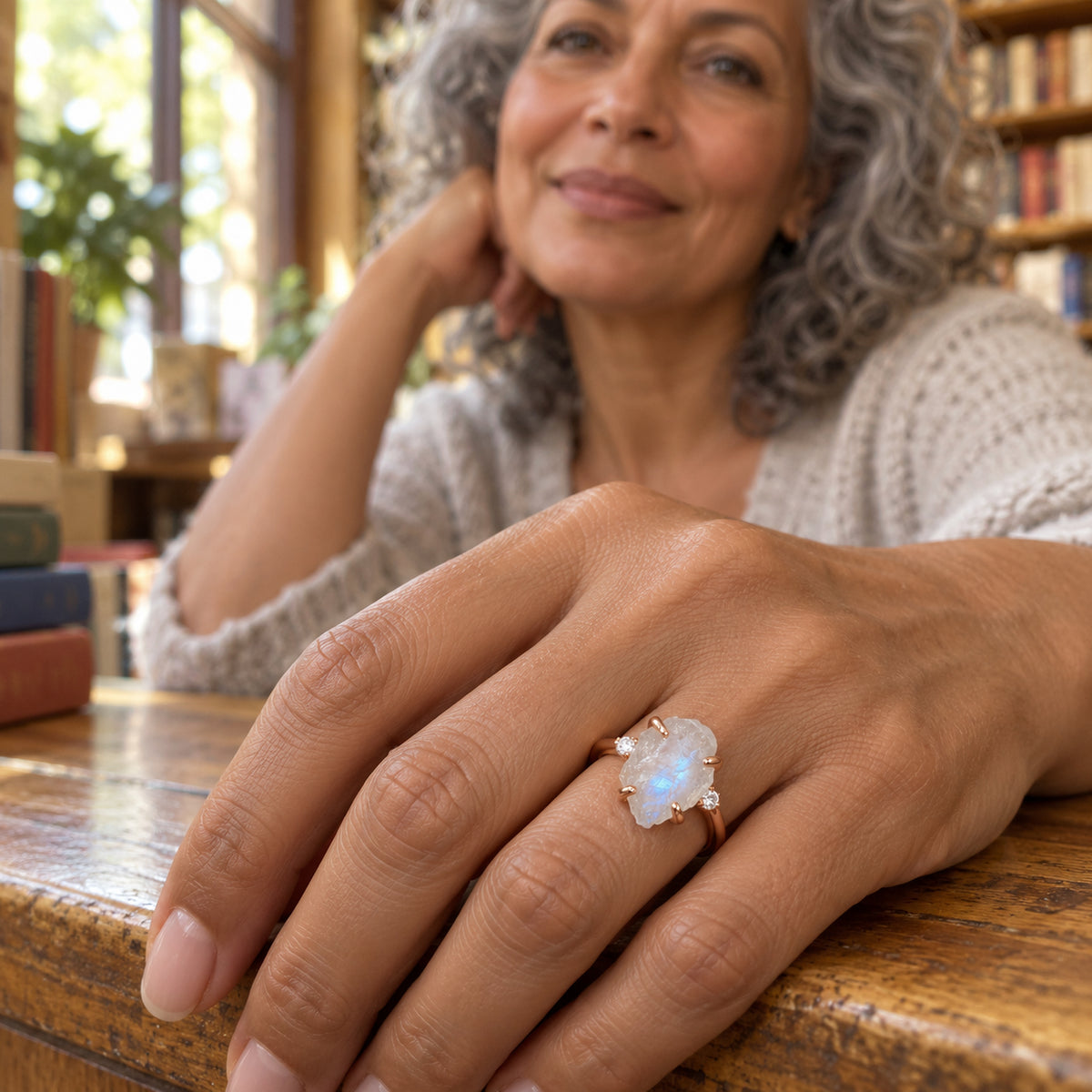 A woman with gray curls wears the rose gold moonstone ring with her hand resting on a wooden counter in a bookshop.