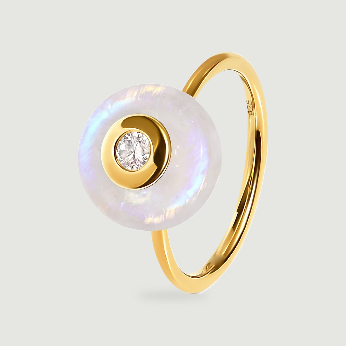 A yellow gold vermeil ring has a round iridescent moonstone disc and a clear central gemstone on a light gray surface.