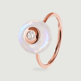 A rose gold vermeil ring displays its circular moonstone face and clear central gemstone against a light gray background.