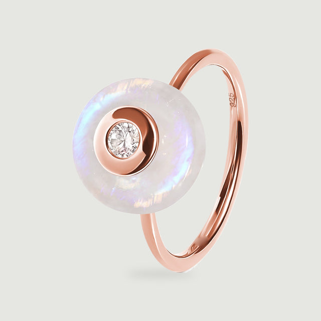A rose gold vermeil ring displays its circular moonstone face and clear central gemstone against a light gray background.