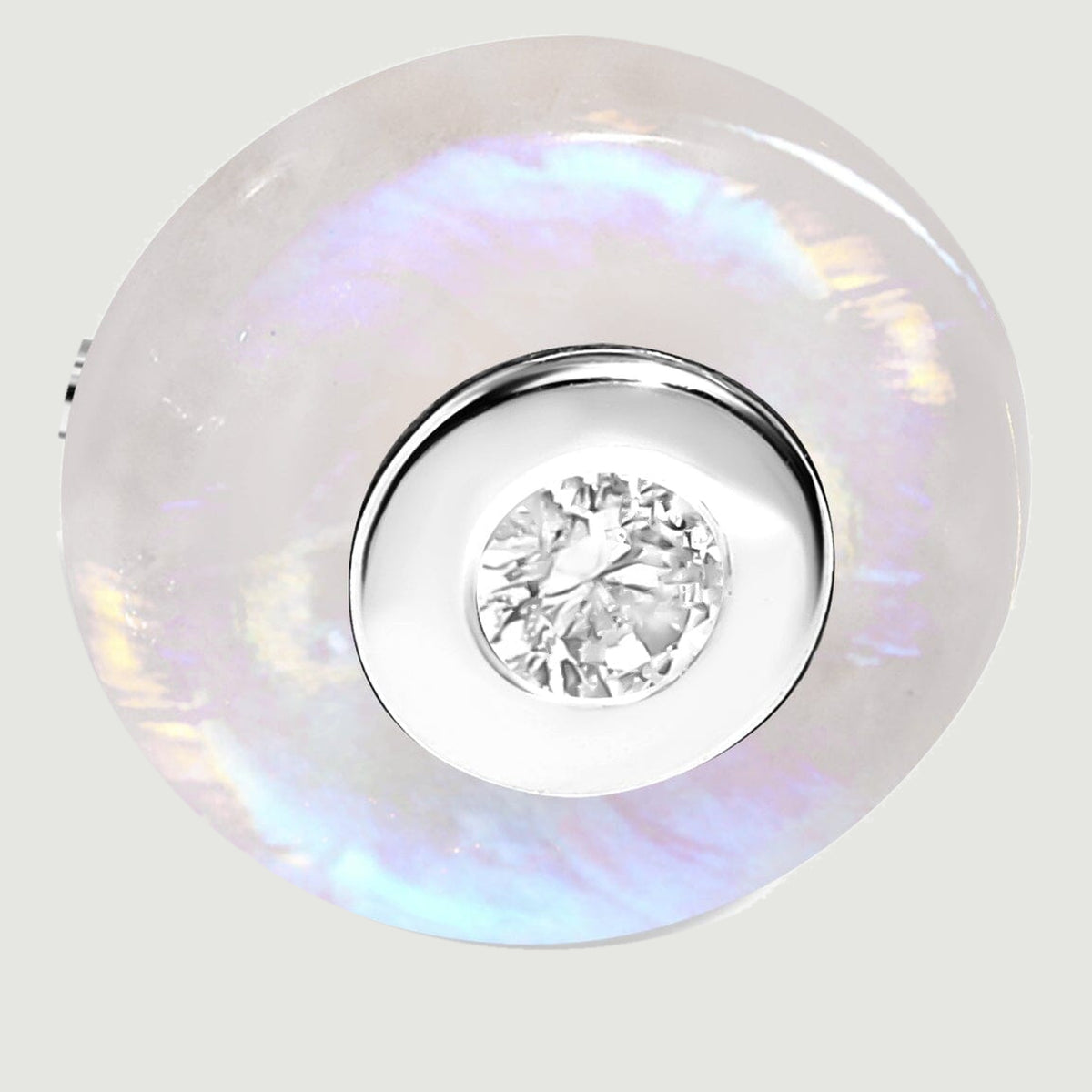 The silver circular bezel and faceted clear gemstone sit inside a moonstone disc with blue and lavender reflections.
