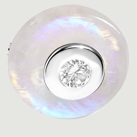 The silver circular bezel and faceted clear gemstone sit inside a moonstone disc with blue and lavender reflections.
