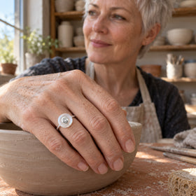 A sterling silver moonstone ring is worn on a hand resting on a clay bowl in a pottery workshop.