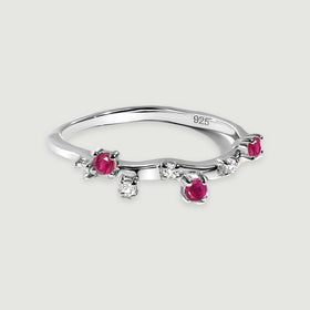 A sterling silver ring with round pink-red and clear stones rests on a light grey surface.