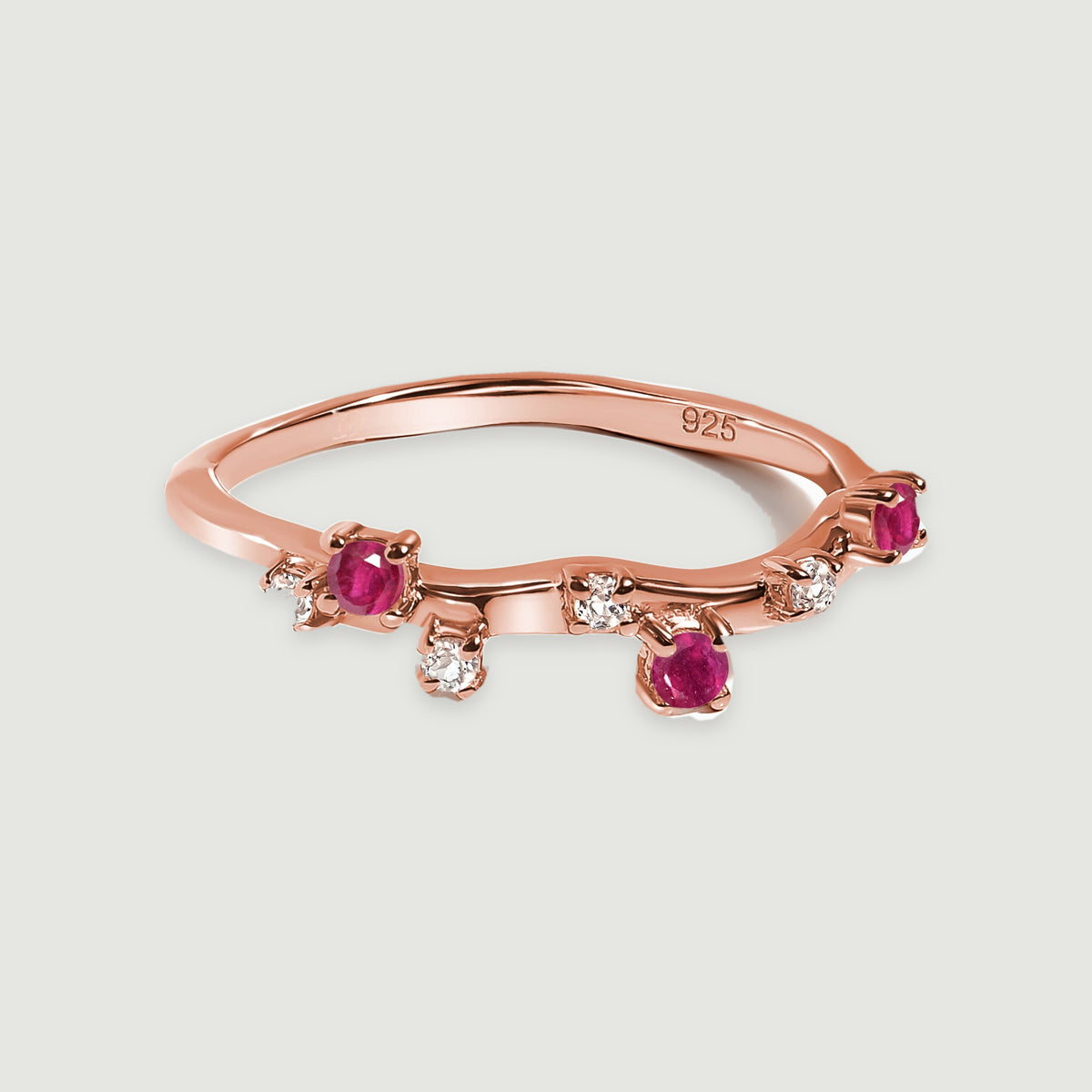 A rose gold vermeil ring displays its curved band and alternating pink-red and clear stone settings.