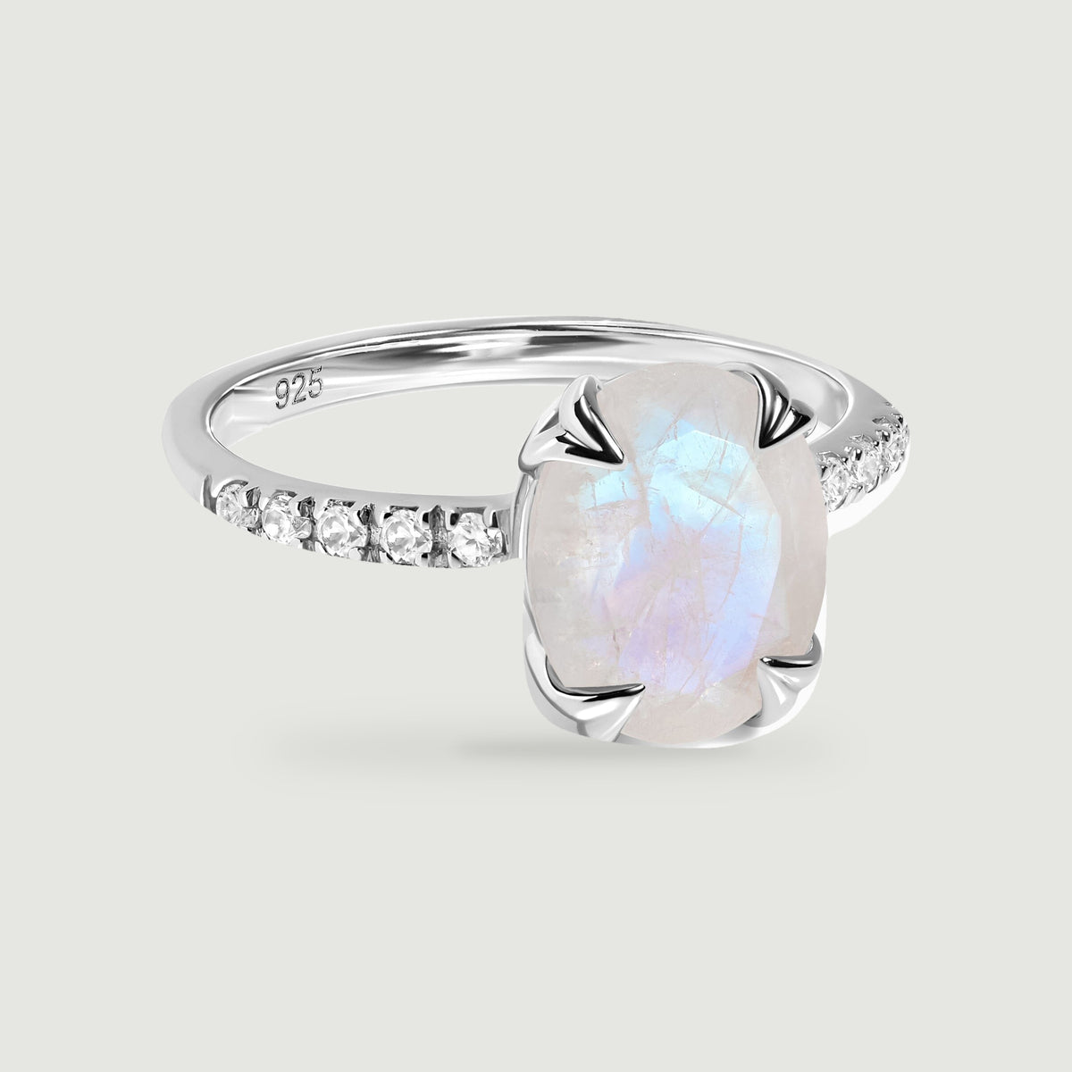 A sterling silver ring with an oval moonstone and clear stones along the band rests on a light gray surface.