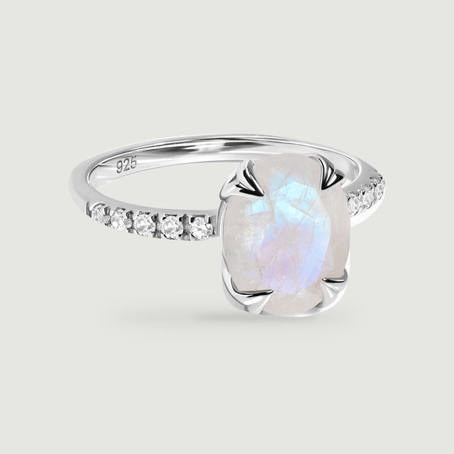 A sterling silver ring with an oval moonstone and clear stones along the band rests on a light gray surface.