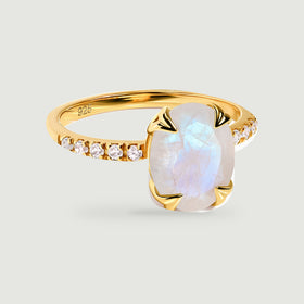 A yellow gold vermeil ring shows an oval moonstone held by four sculpted prongs above a stone-set band.