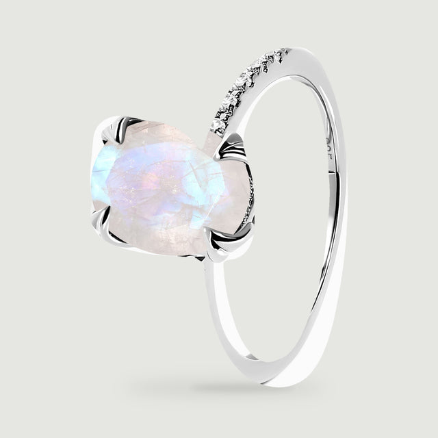An angled sterling silver ring reveals its curved band, raised moonstone setting, and rows of clear stones.