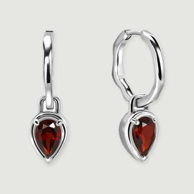 A pair of silver-tone hoops with red teardrop garnets is centered over a soft contact shadow.