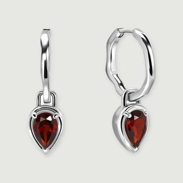 A pair of silver-tone hoops with red teardrop garnets is centered over a soft contact shadow.