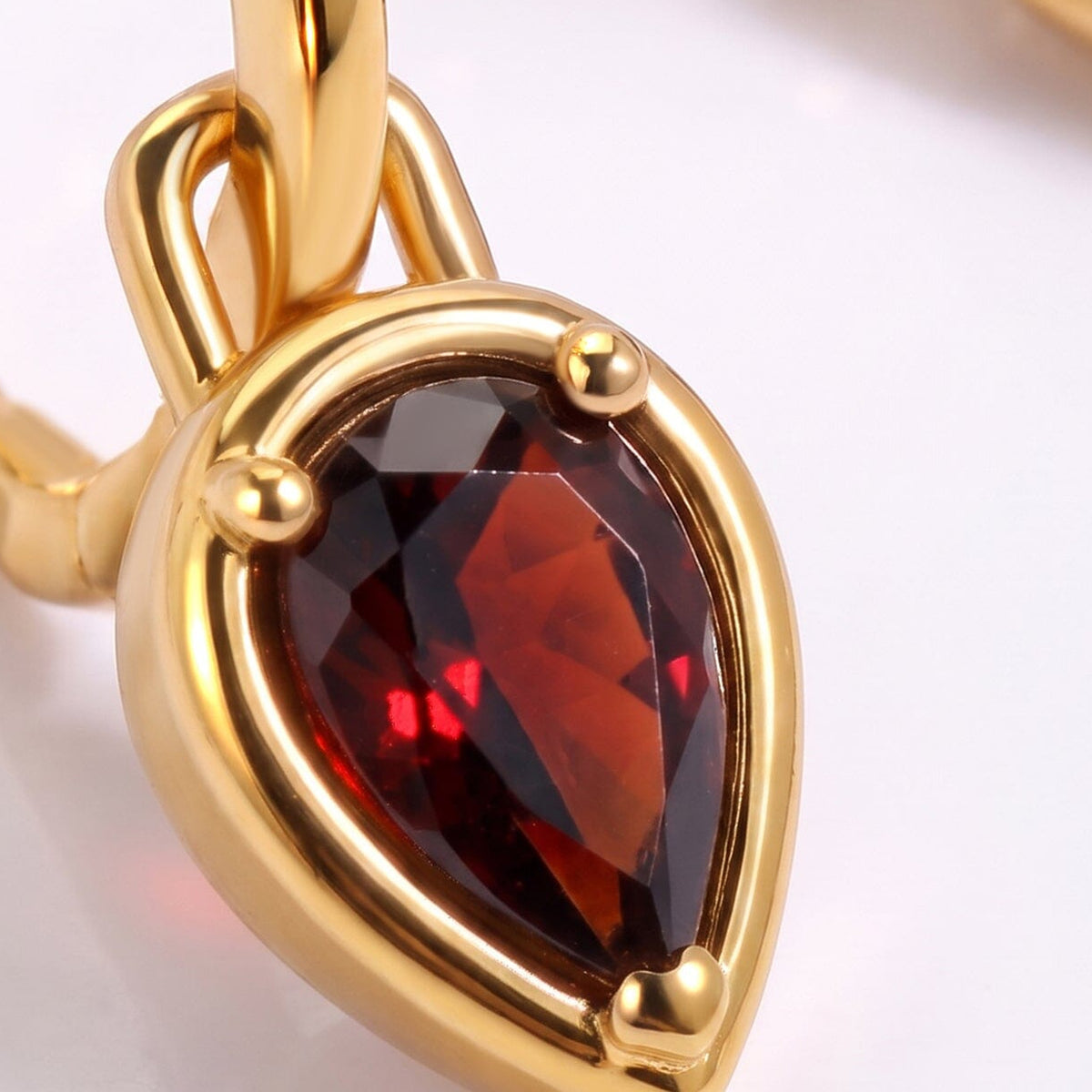 A faceted red garnet and three rounded prongs fill the foreground beside a polished gold hoop.