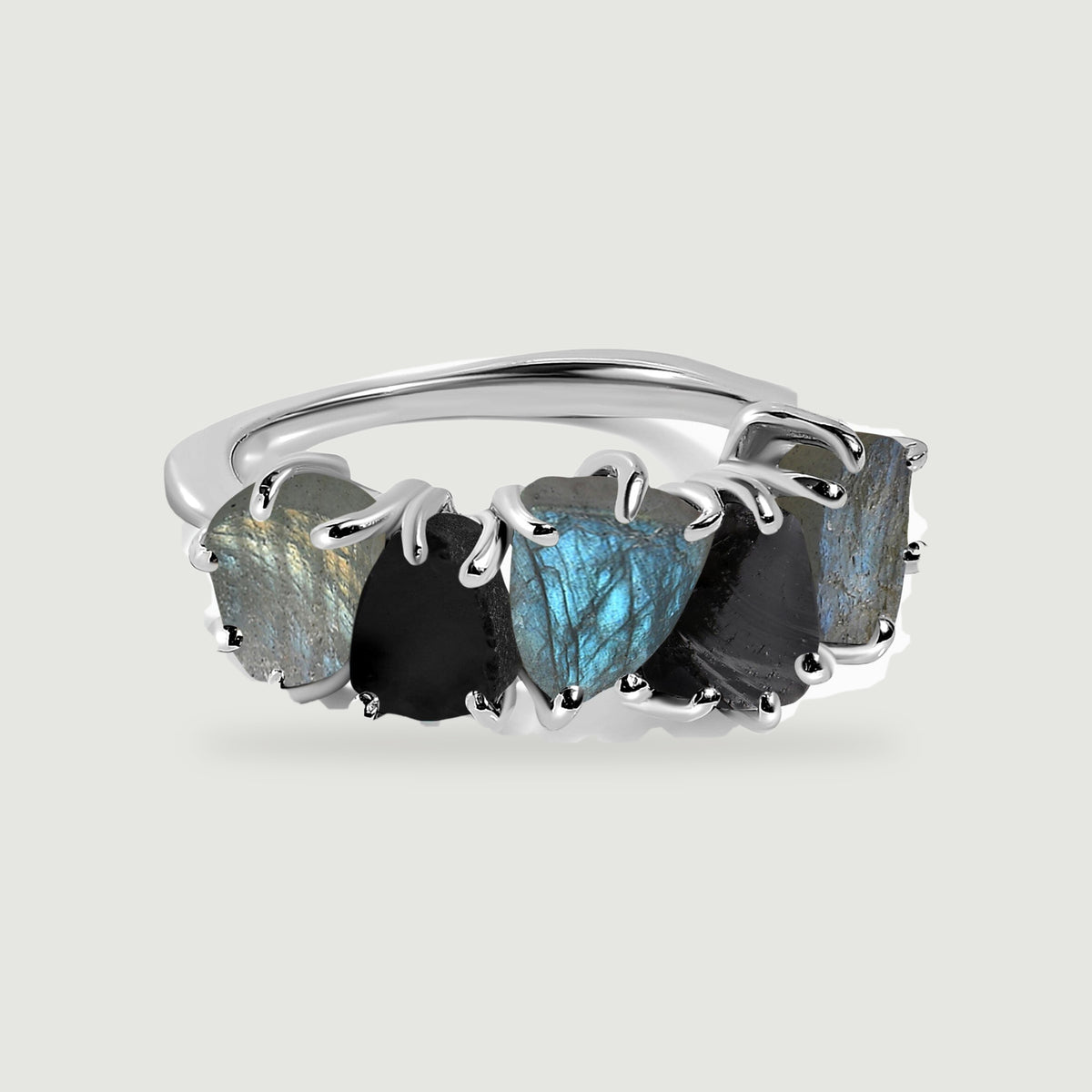A silver-tone ring displays five alternating raw labradorite and black obsidian stones on a pale gray surface.