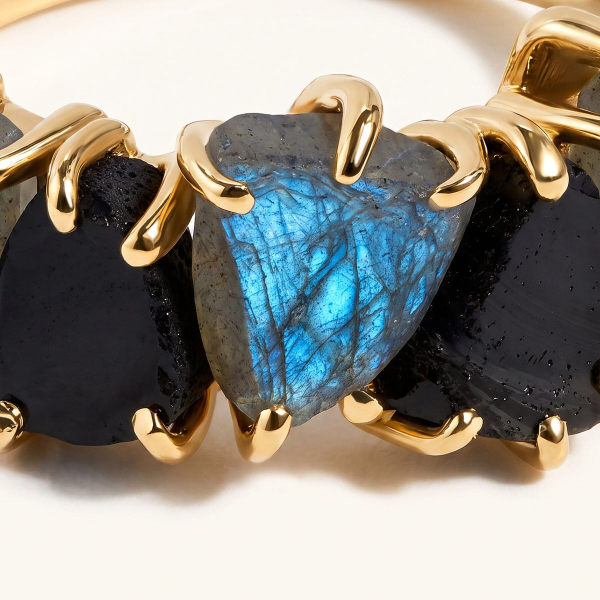 Yellow gold-tone claws frame the blue surface of a raw labradorite and the dark stones beside it.